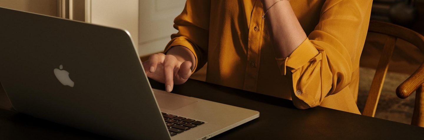 A person in a yellow shirt uses a laptop to book a flight.