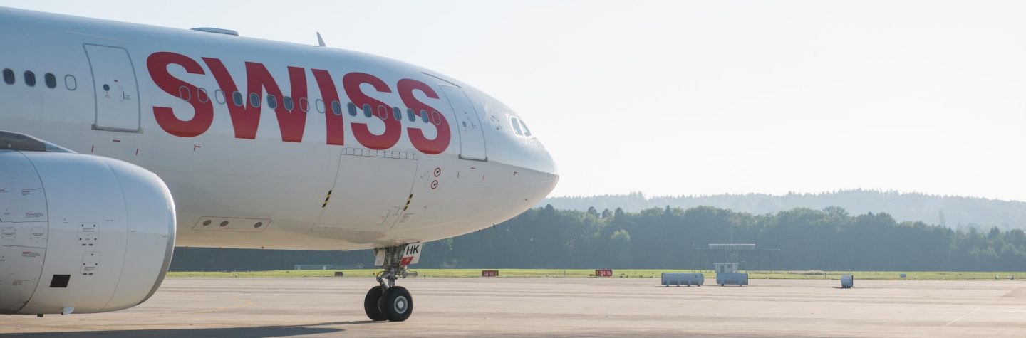 Swiss airplane on sunny tarmac with trees.
