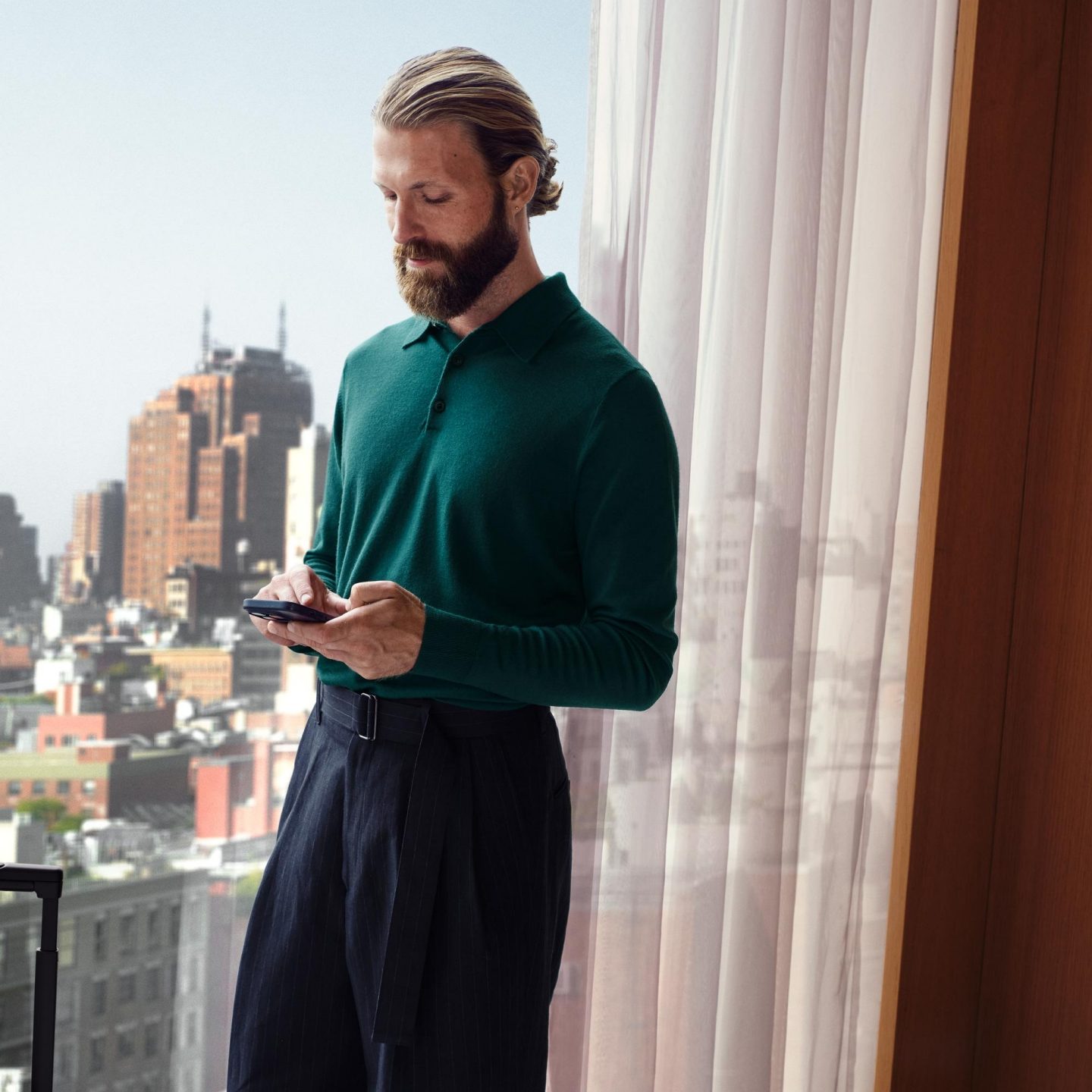 A man standing by a window looking at his smartphone.