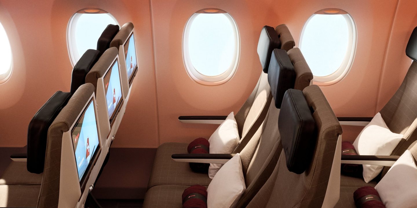 Interior cabin view of SWISS aircraft seats with screens, pillows, and warm ambient lighting.