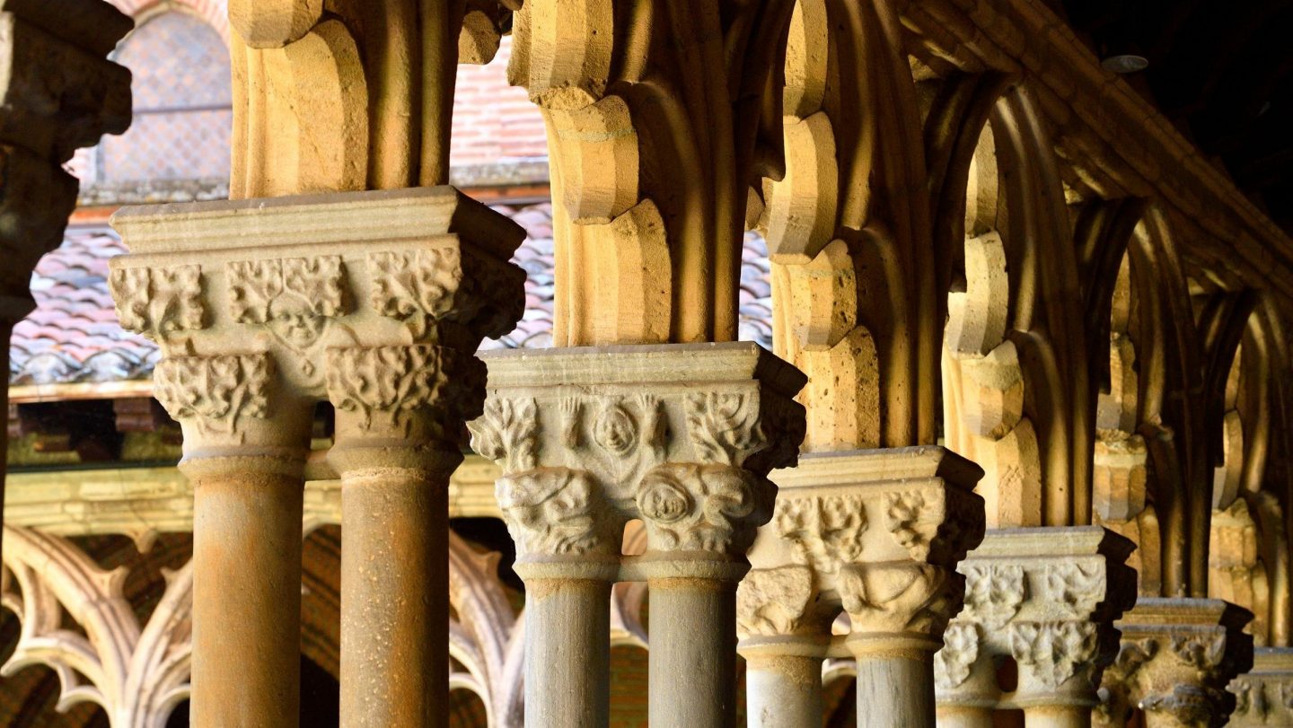 A sunlit row of carved stone columns supports an ornate arcade that recedes into shadow.
