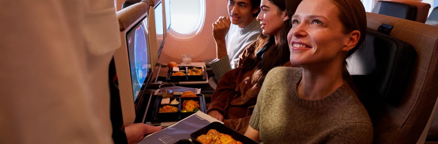 A flight attendant serves a meal to a passenger in economy class.