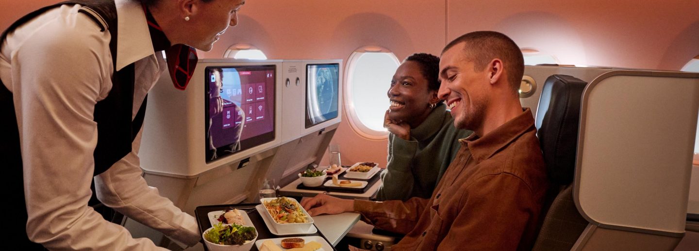 A SWISS flight attendant serving a meal to two smiling passengers in Premium Economy.