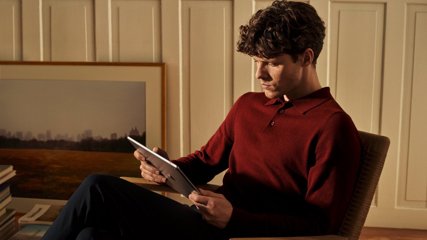 Un homme assis sur une chaise regardant vers le bas un écran de tablette.