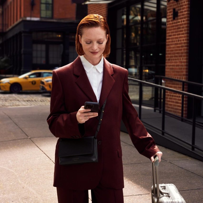 Femme avec un smartphone et une valise à roulettes dans une rue de la ville.