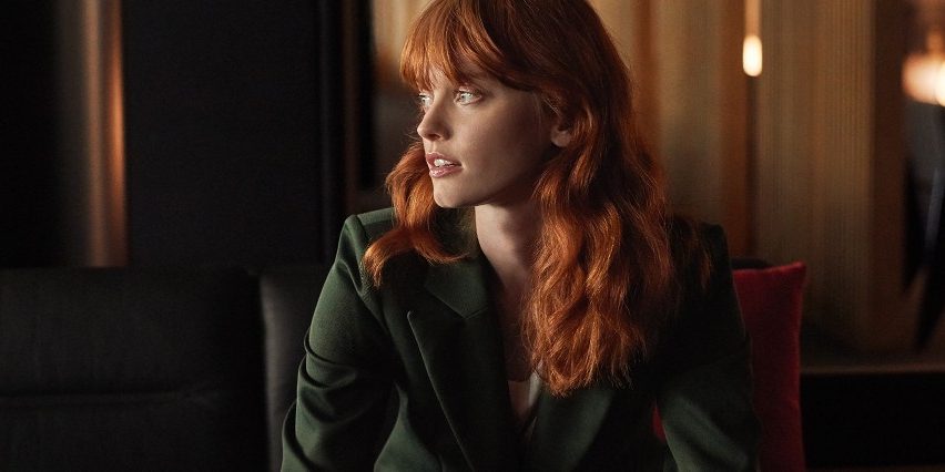 A woman sitting inside a modern airport lounge looking toward a window.