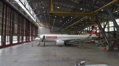 In the large hangar hall, two mechanics are seen working on an Airbus A320neo.