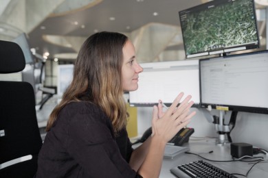 NOC manager Angela is seen in side profile, sitting in front of her desk. the desk is equipped with 4 screens, one of which is on top of the other three. it shows a map. 