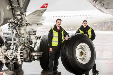 Two SWISS Technics standing next to the wheel that they have exchanged