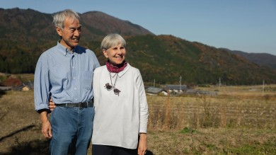 Regina and Shunichi standing next to each other in a rural setting and smiling.