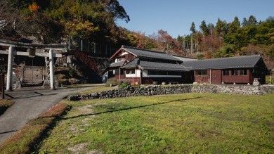 An old farmhouse surrounded by lawns and forest.
