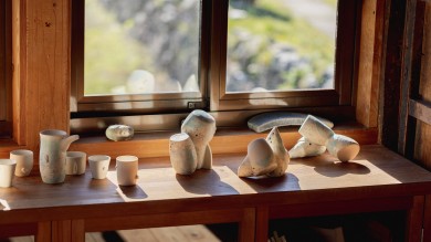 Vessels assmbled on a wooden table in front of a window, through which sunlight falls on parts of the vessels.