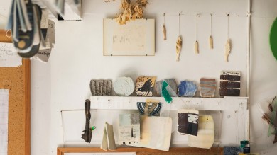 Shelves mounted on a white wall display different works by Regina.