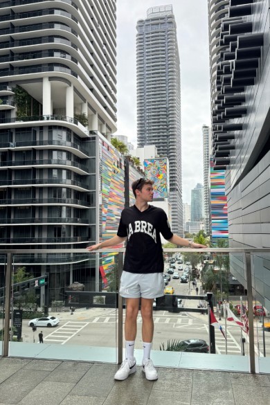 Yanic posiert stolz an seinem Lieblings-Fotospot auf der Brücke zwischen zwei Gebäuden beim Brickell City Centre, umgeben von hohen Wolkenkratzern.